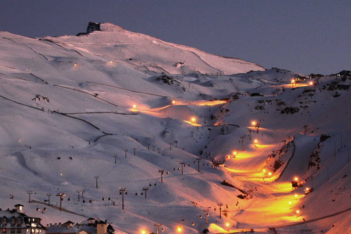 Montanha coberta de neve, com teleféricos e alguns edifícios na base.