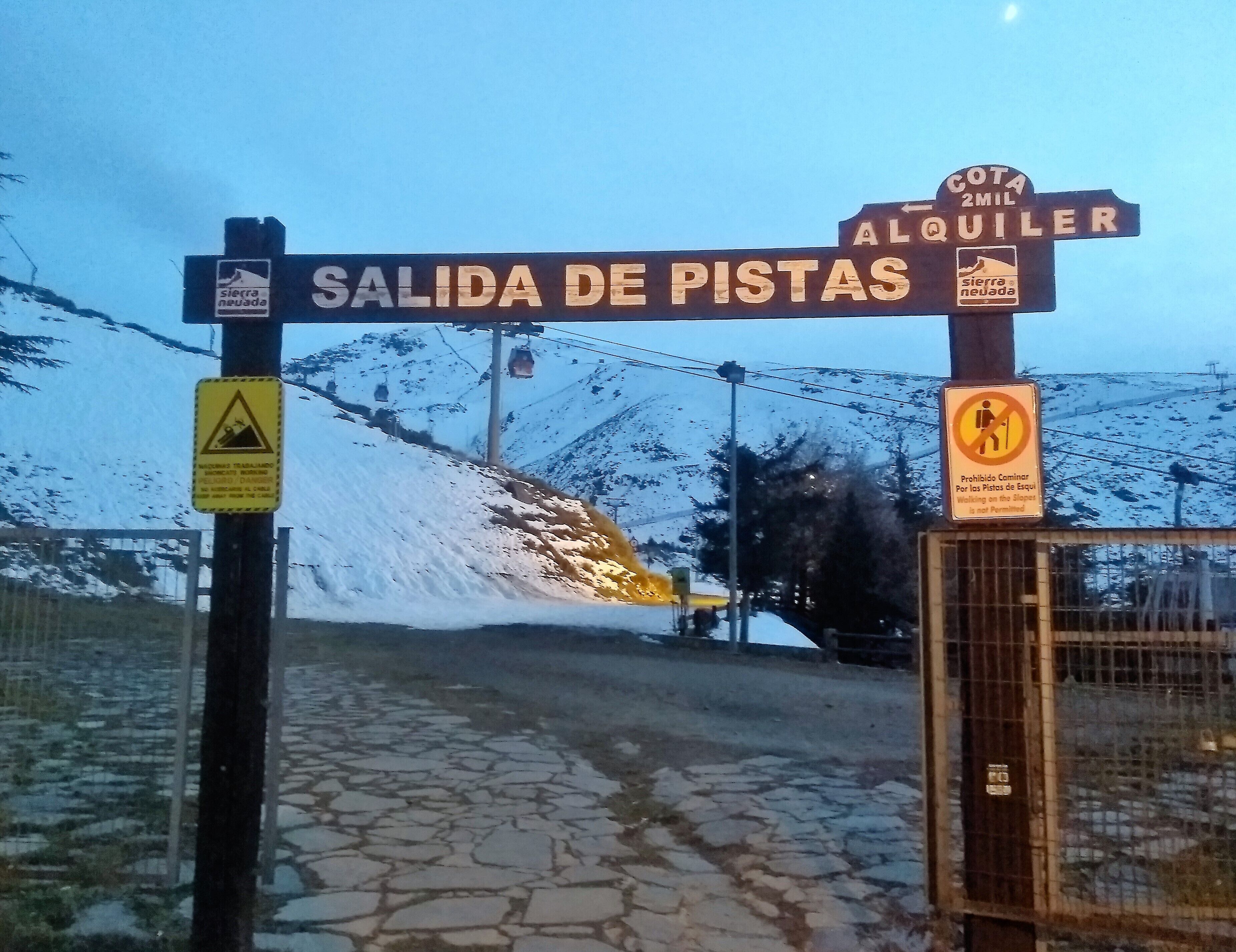 Un cartel con 'SALIDA DE PISTAS' y 'ALQUILER' que indica una zona de alquiler, con un letrero de advertencia sobre caminar por las laderas.