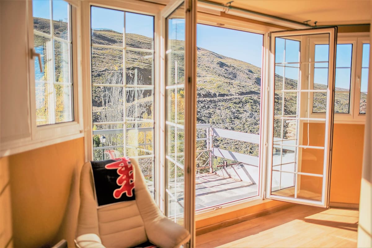 Quarto com amplas janelas oferecendo vista para uma paisagem montanhosa.