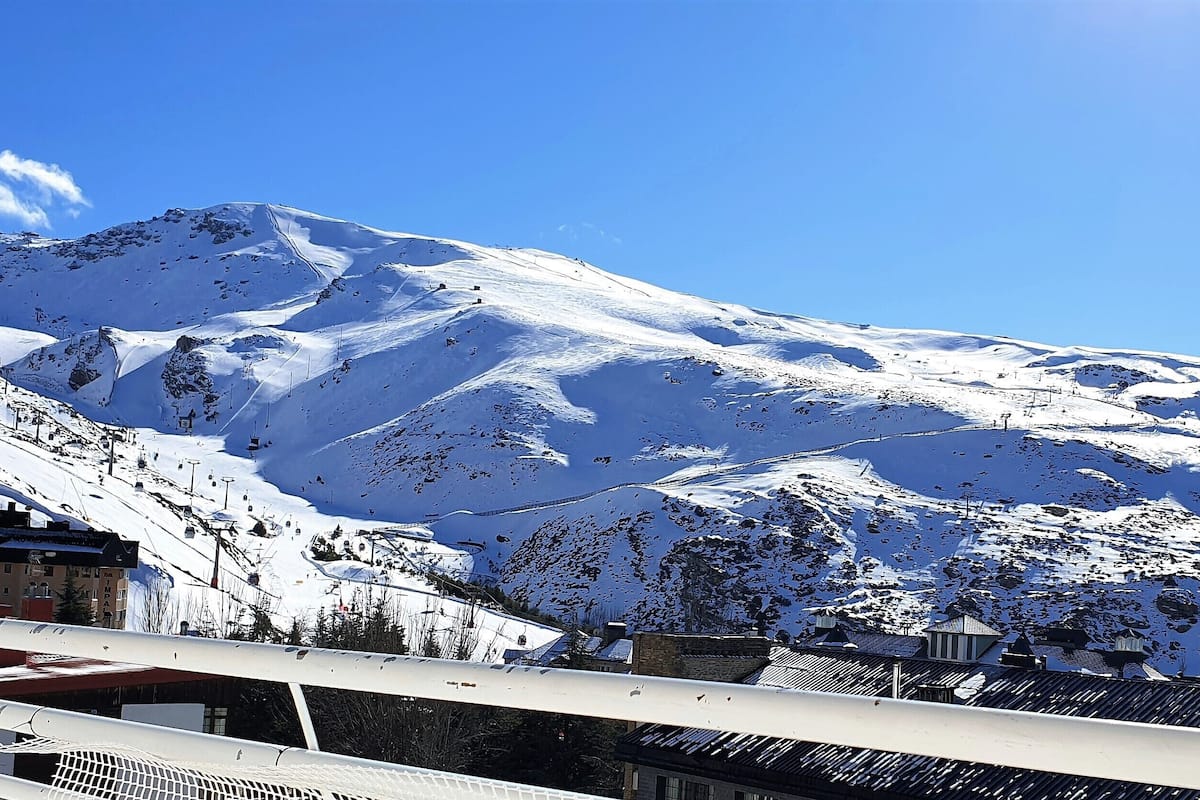 Montanha coberta de neve com um teleférico e edifícios na base.