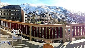 Un balcón con vistas a montañas nevadas y un edificio con múltiples ventanas.