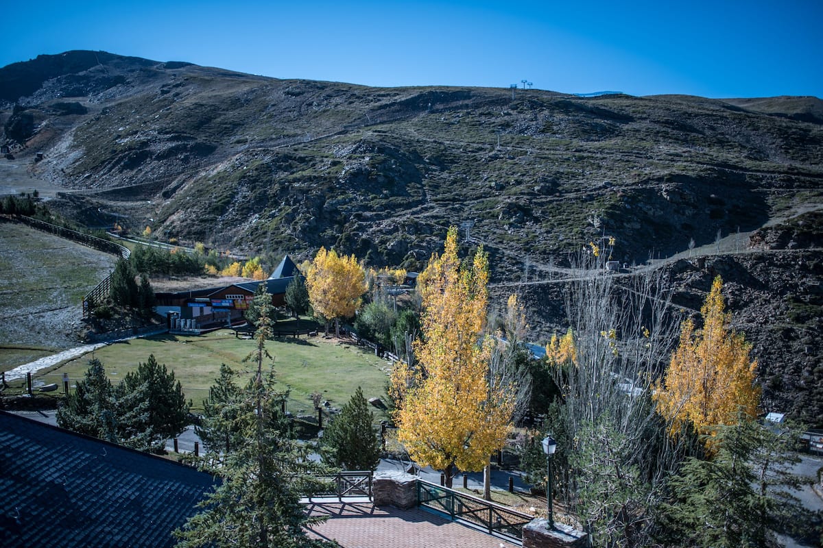 Paisagem montanhosa com um edifício rodeado de árvores com folhagem de outono.