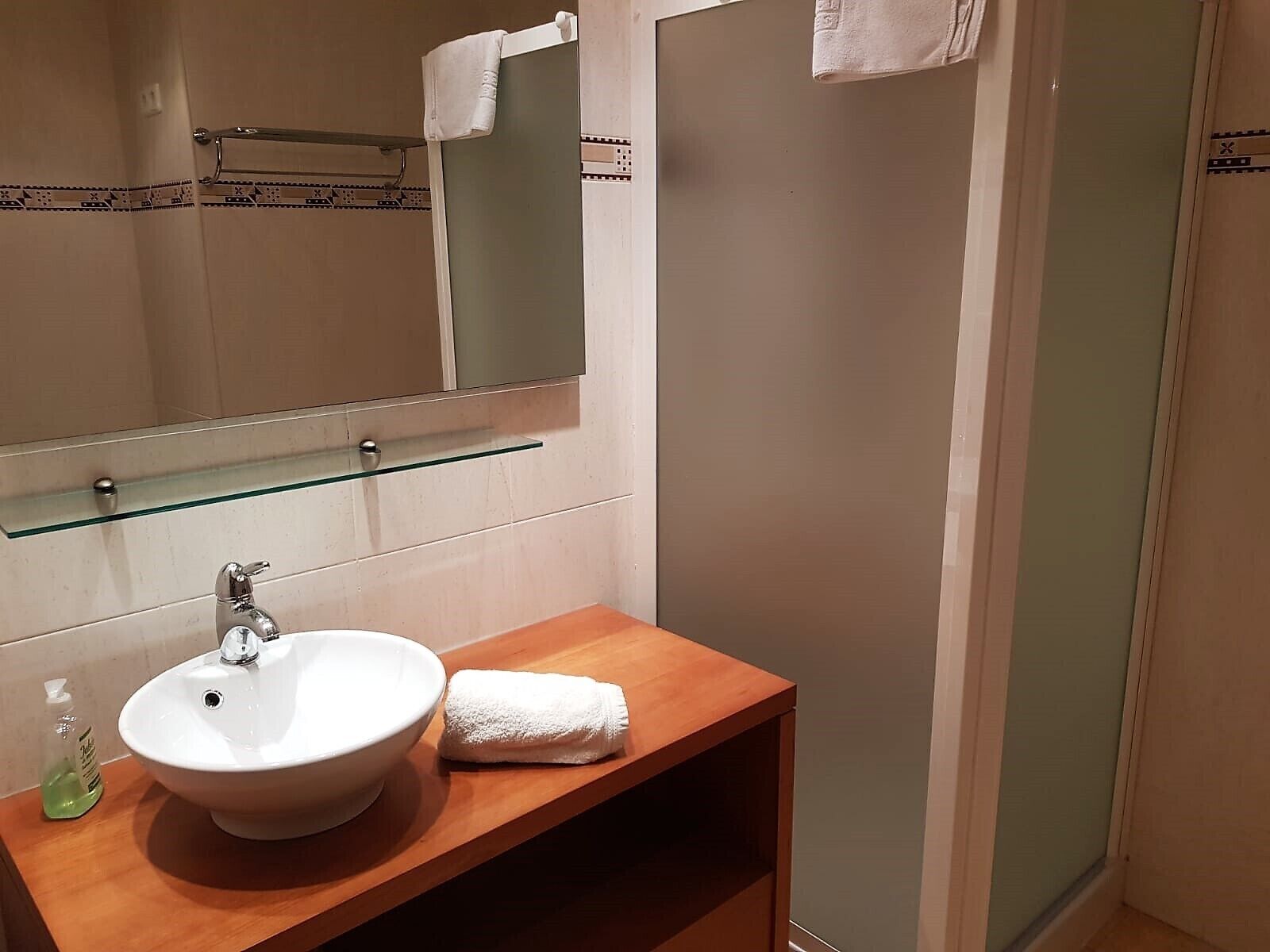 Un bany amb un lavabo blanc, una prestatgeria de vidre a sobre i una tovallola penjada en un suport.
