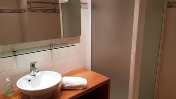 Une salle de bain avec un lavabo blanc, une étagère en verre au-dessus et une serviette suspendue à un porte-serviettes.