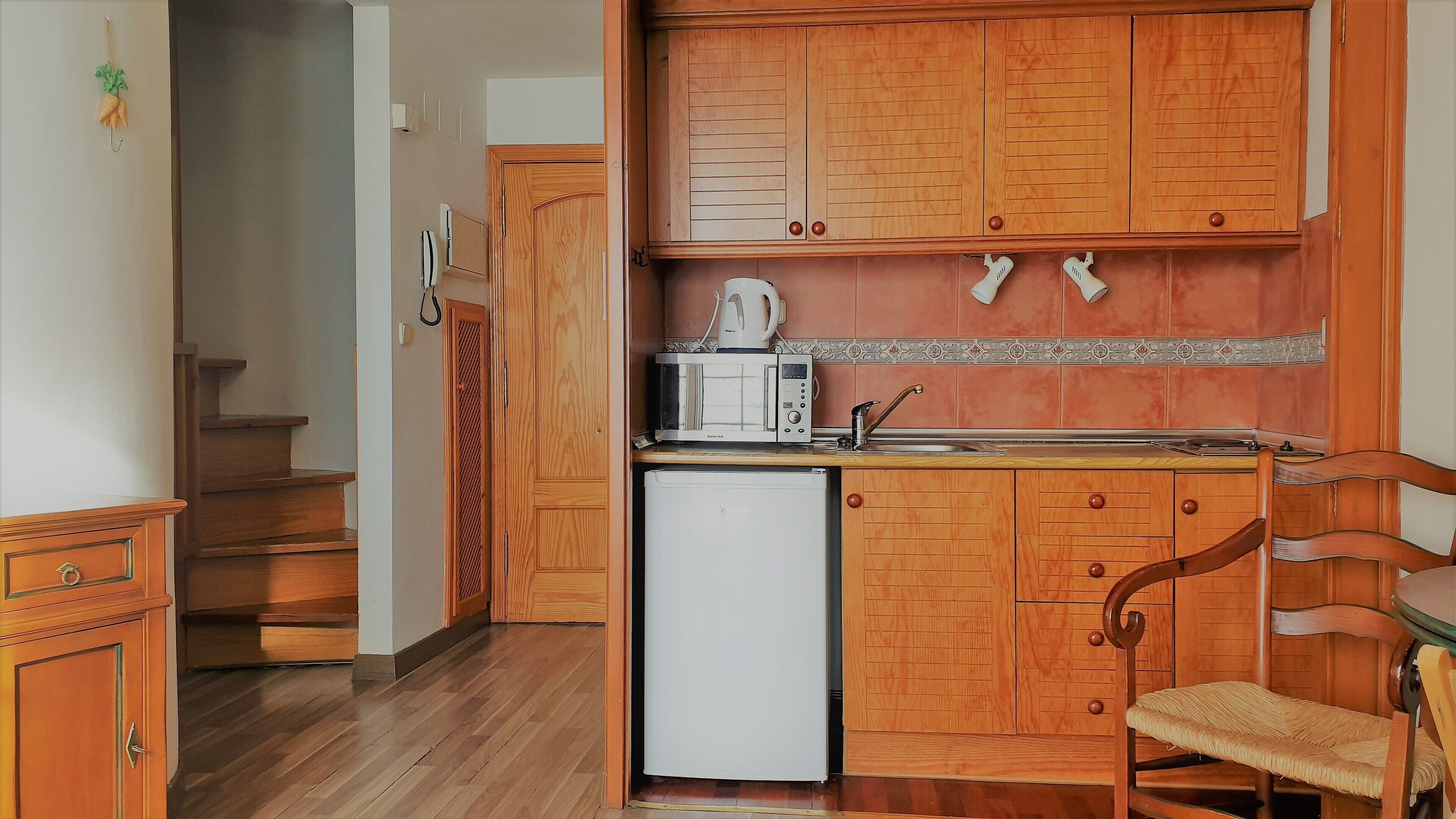 Una cocina compacta con armarios de madera, un microondas, una cafetera y un refrigerador pequeño.