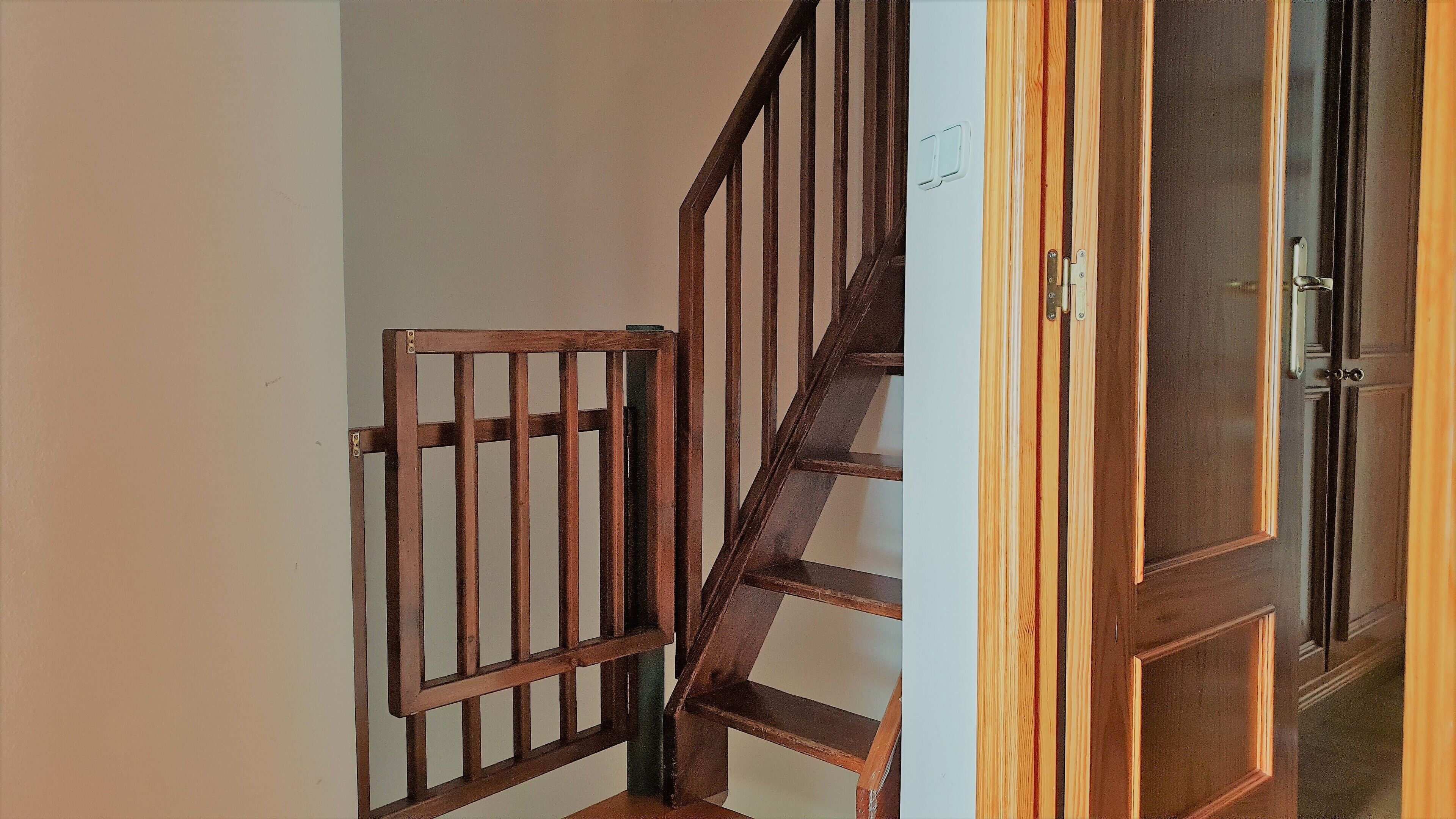 Eine Holztreppe mit einem Metallgitter am oberen Ende, die zu einem Raum mit einer Tür führt.