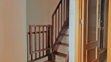 Eine Holztreppe mit einem Metallgitter am oberen Ende, die zu einem Raum mit einer Tür führt.