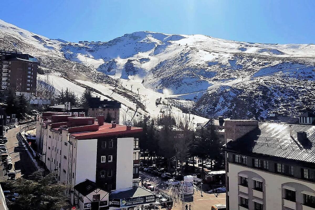 Uma cidade montanhosa com picos cobertos de neve, edifícios com telhados vermelhos e um teleférico no vale.