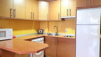 Una cocina compacta con armarios de madera, un microondas, un hervidor y un refrigerador.