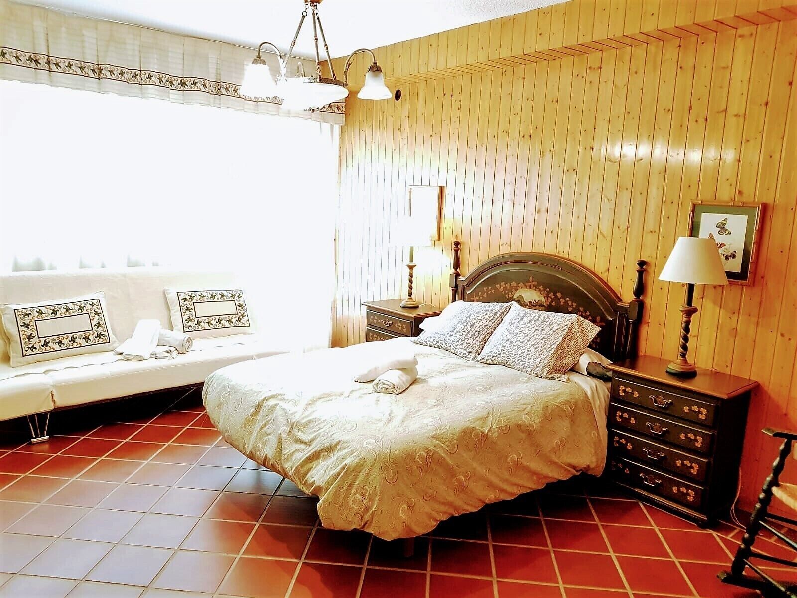 Un dormitorio con cama, mesitas de noche, cómoda y ventana con cortinas.