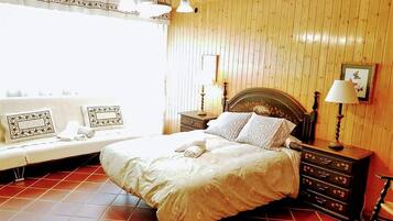 Un dormitorio con cama, mesitas de noche, cómoda y ventana con cortinas.