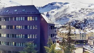 Un edificio moderno de varios pisos y grandes ventanales, rodeado de montañas nevadas.