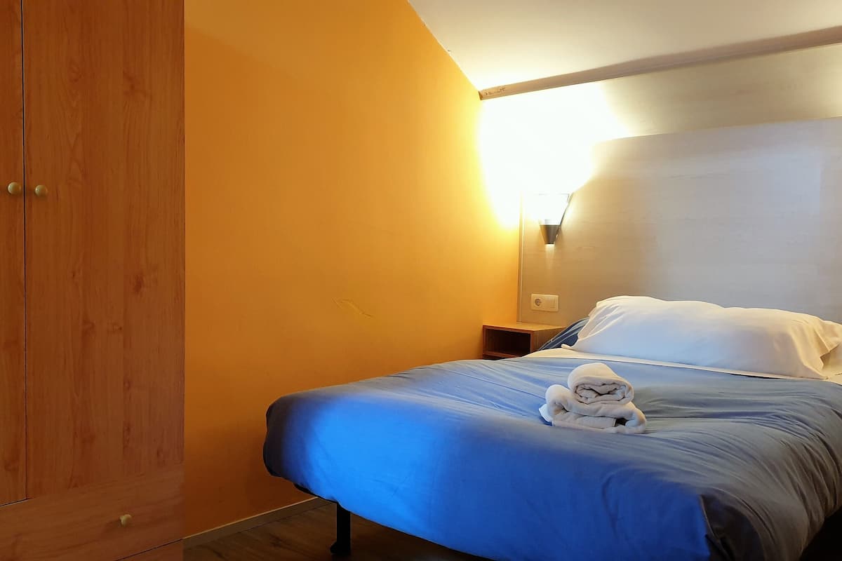 Quarto de hotel com guarda-roupa de madeira, cama com roupa de cama azul e luminária fixada na parede.