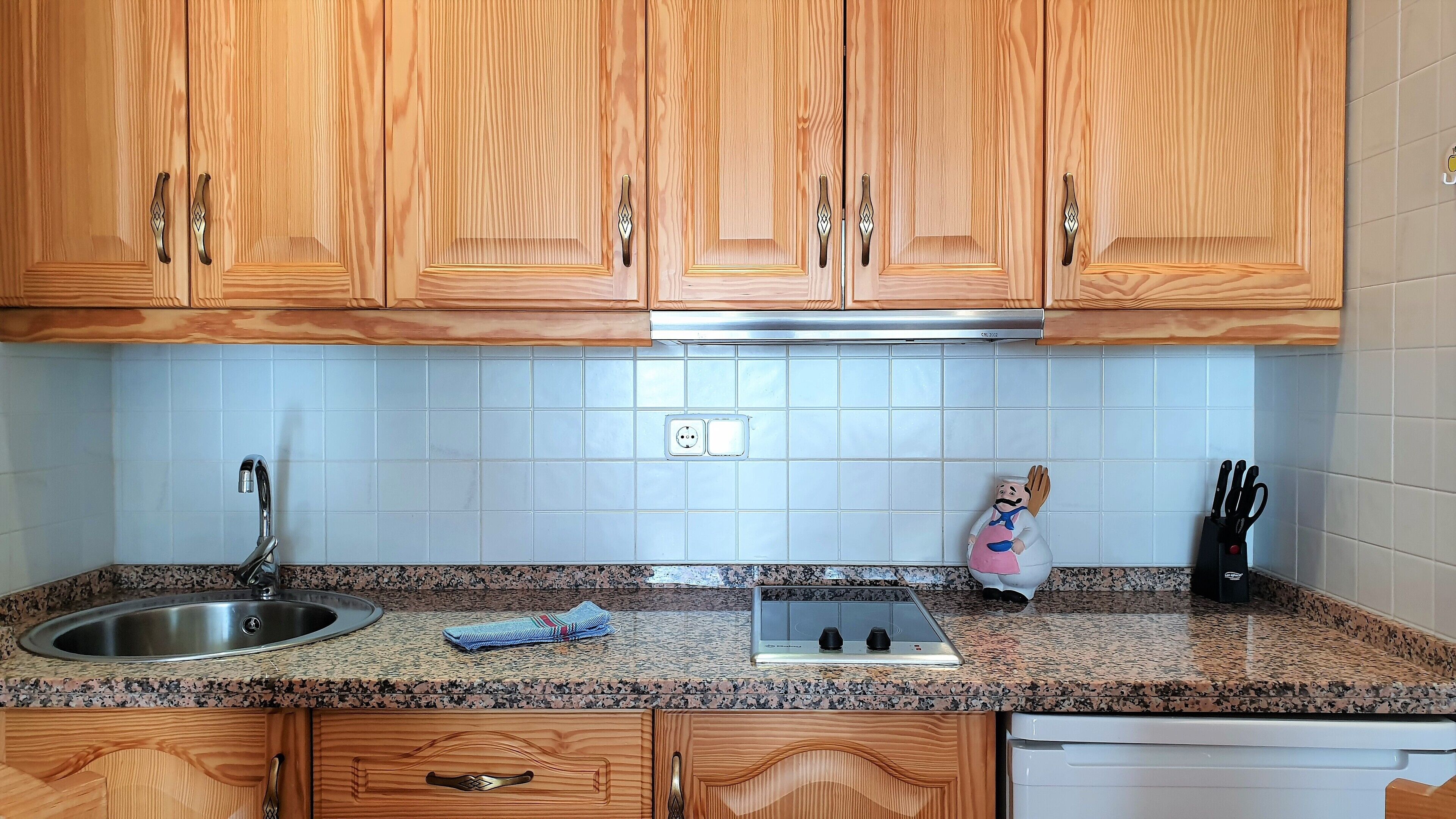 A kitchen with wooden cabinets, a granite countertop, a stainless steel sink, a stove, and a dish rack.