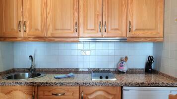Una cucina con mobili in legno, un piano di lavoro in granito, un lavello in acciaio inossidabile, un fornello e un espositore per piatti.