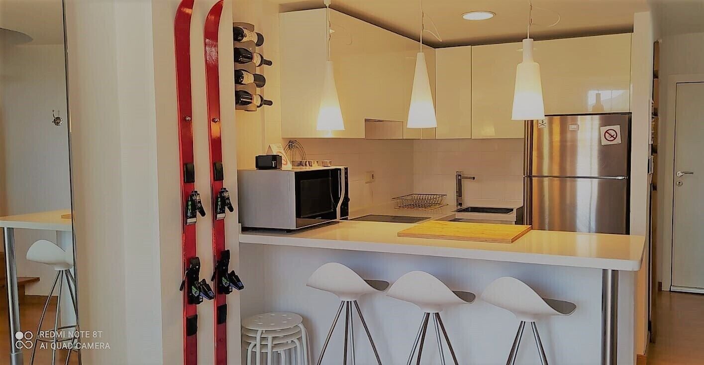 Una cocina moderna con microondas, refrigerador de acero inoxidable, lámparas colgantes y una barra con taburetes.