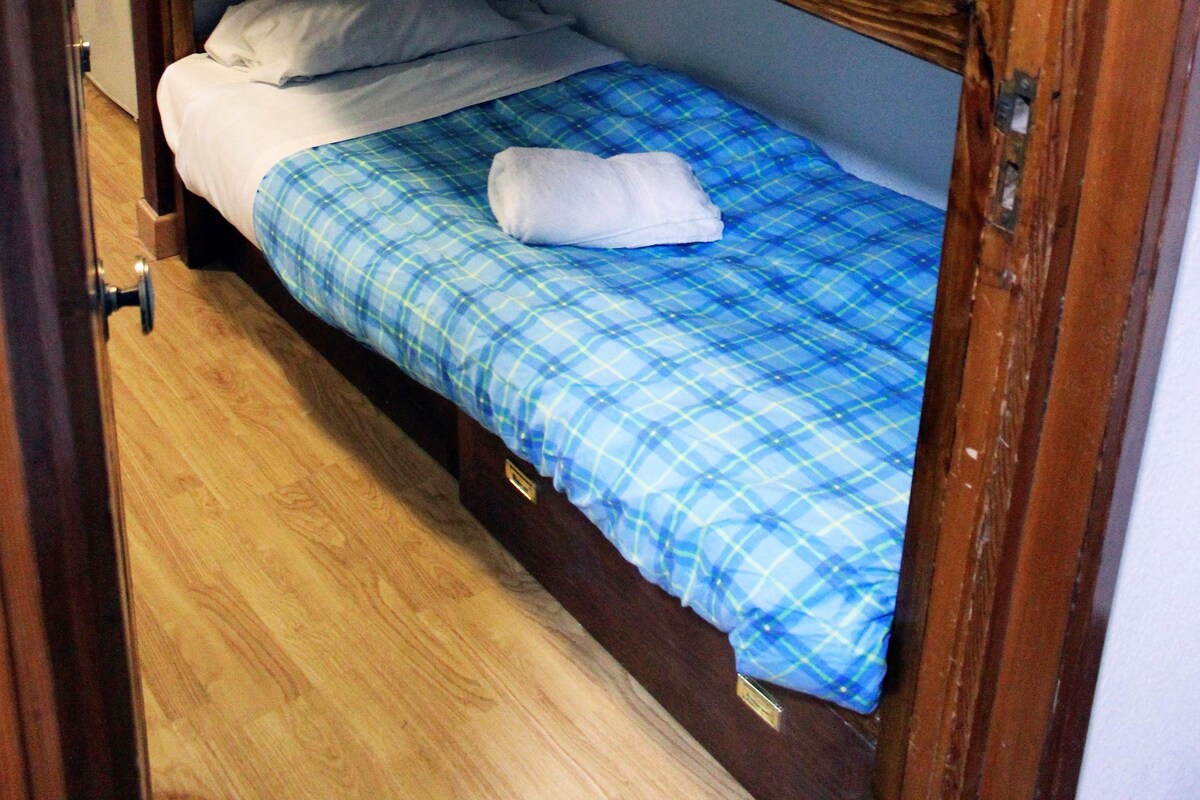 Una cama litera con dos niveles, cada uno con colcha azul a cuadros y almohadas blancas.