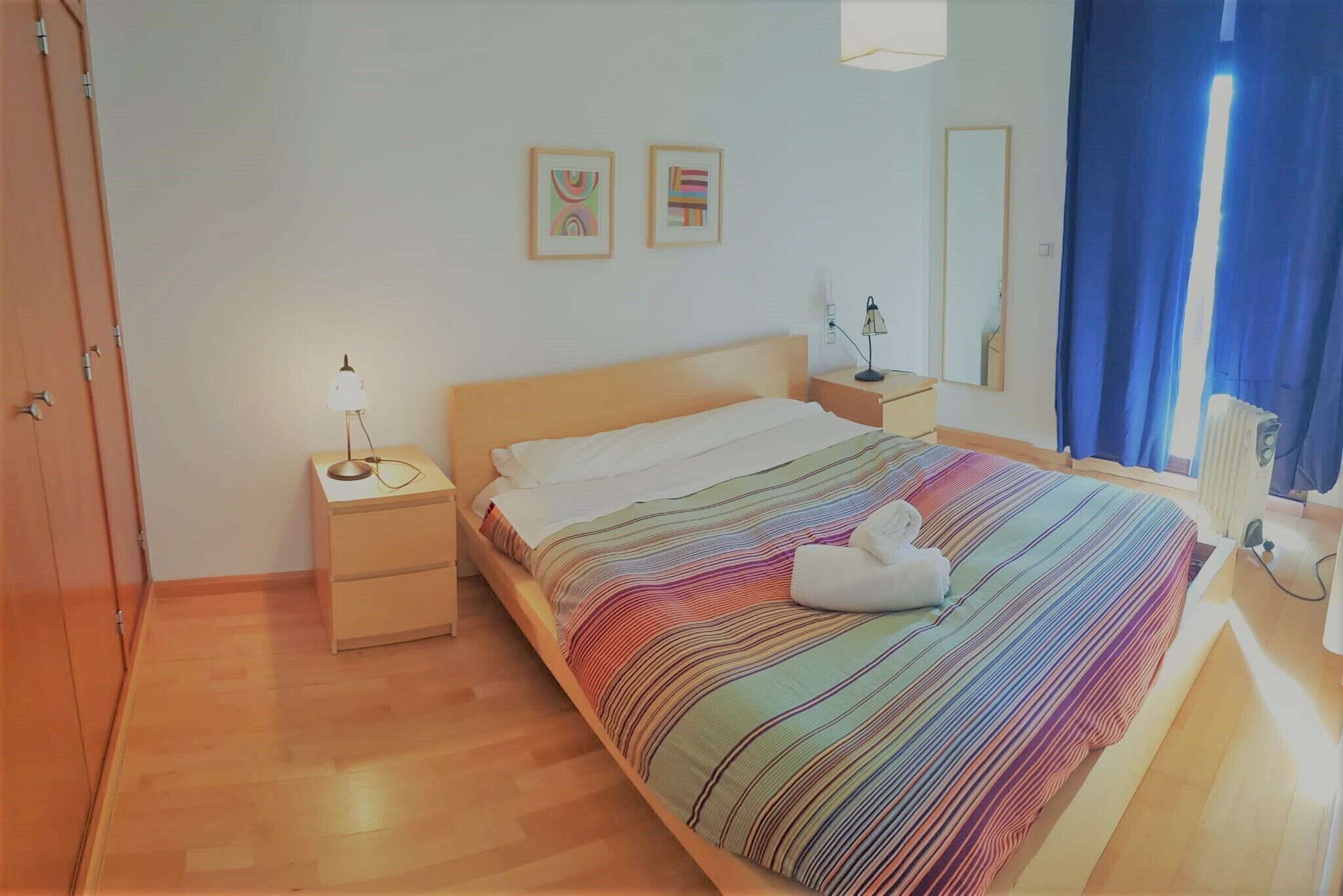 Et soveværelse med seng, et natbord, en lampe, et spejl og et vindue med gardiner.