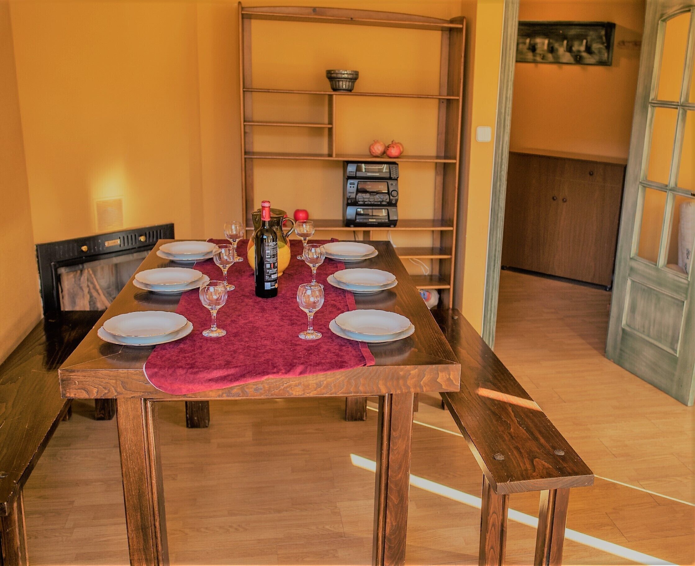 A dining table set with plates, wine glasses, and a bottle, with a red table runner.
