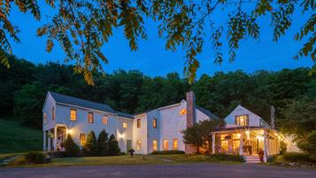 Charming two-story house with a cozy porch and beautifully manicured lawn, surrounded by trees.