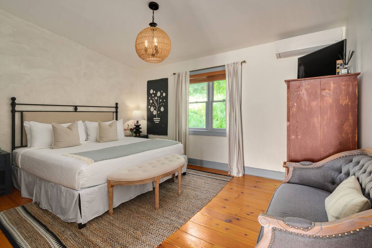 A bedroom with a large bed, a wooden bench, a grey sofa, and a wooden cabinet.