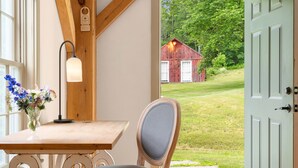 Un intérieur en bois avec une table, une chaise et une vue sur une grange rouge, visible à travers une porte ouverte.