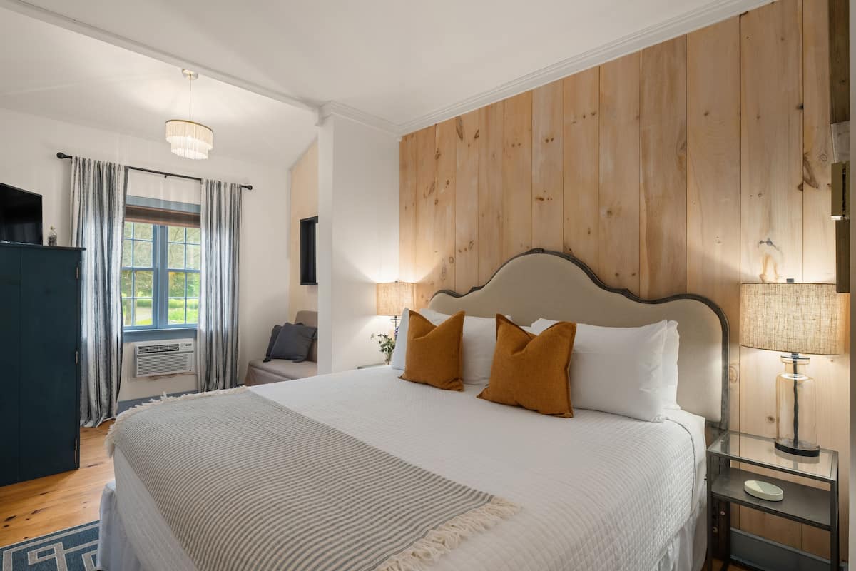 A bedroom with a large bed, wooden panel wall, bedside lamps, and a window with curtains.