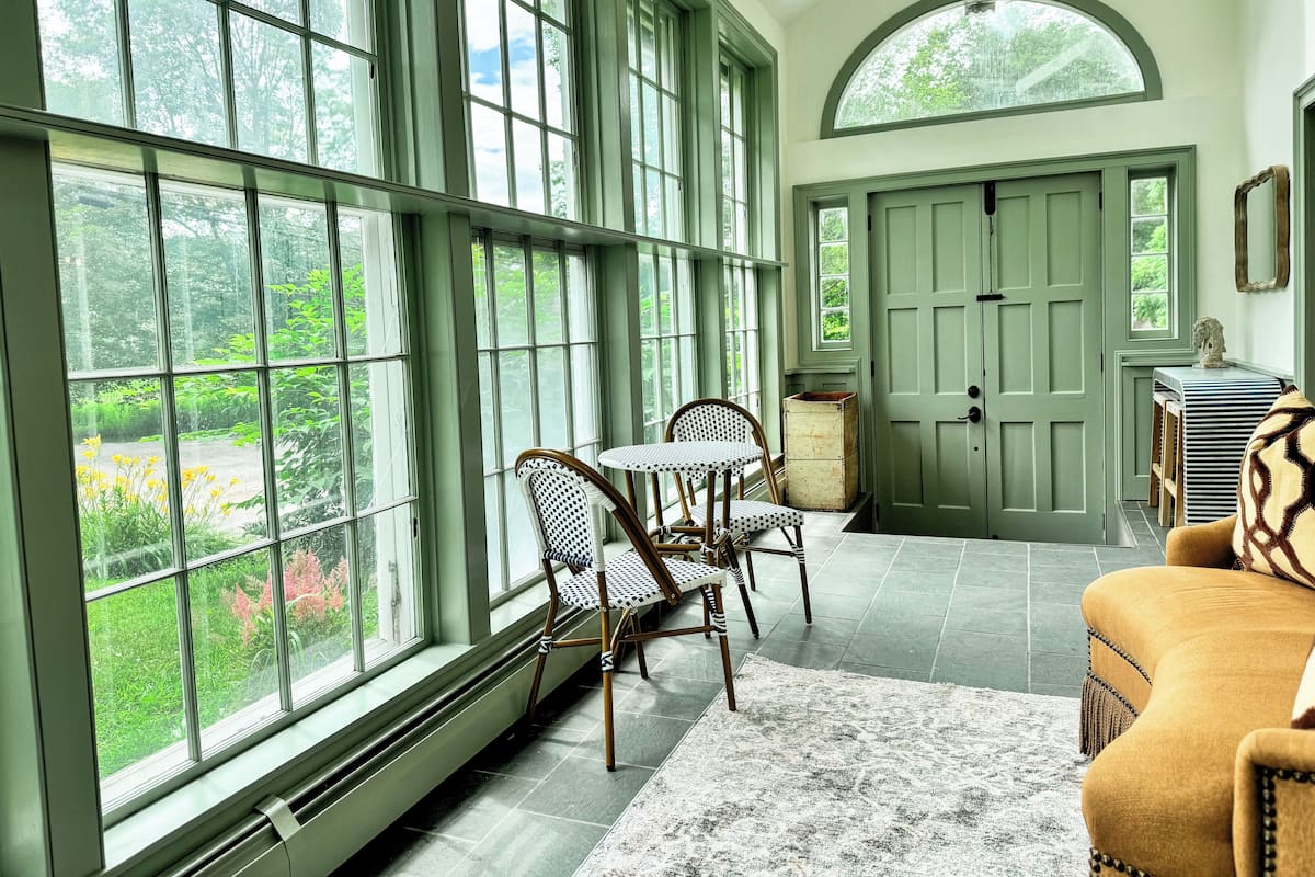 A room with large windows, a door, a table with chairs, and a sofa.