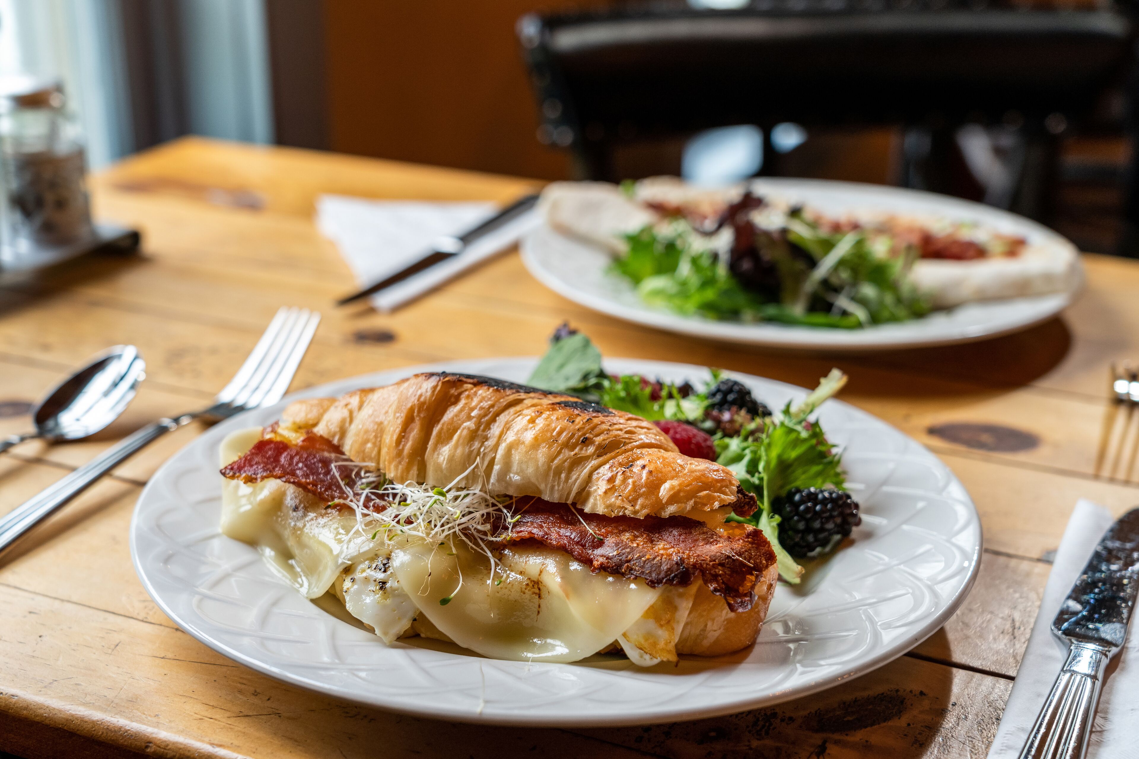 A table with a croissant sandwich, a salad, and a plate of food.