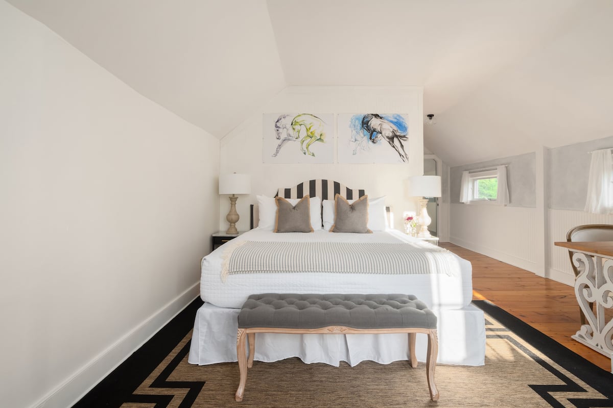 A bedroom with a large bed, a bench, and artwork on the wall.