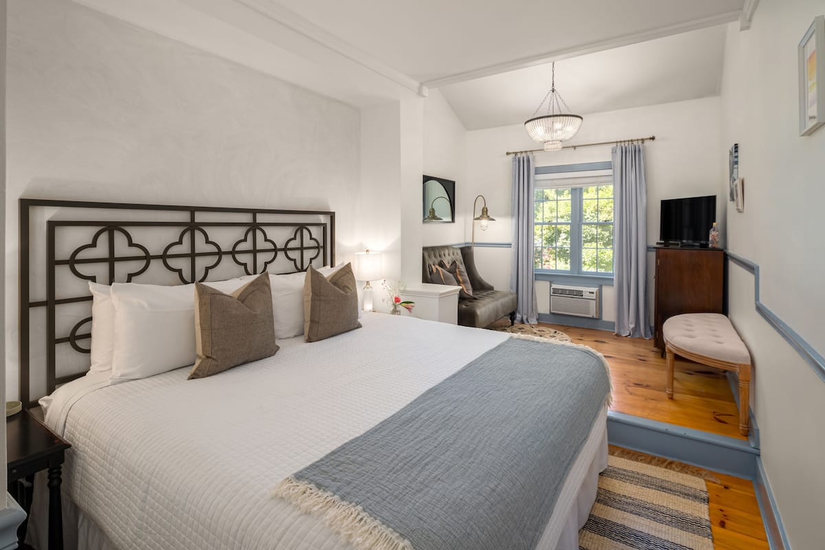 A bedroom with a large bed, a bedside table, a chair, a television, and a window with curtains.