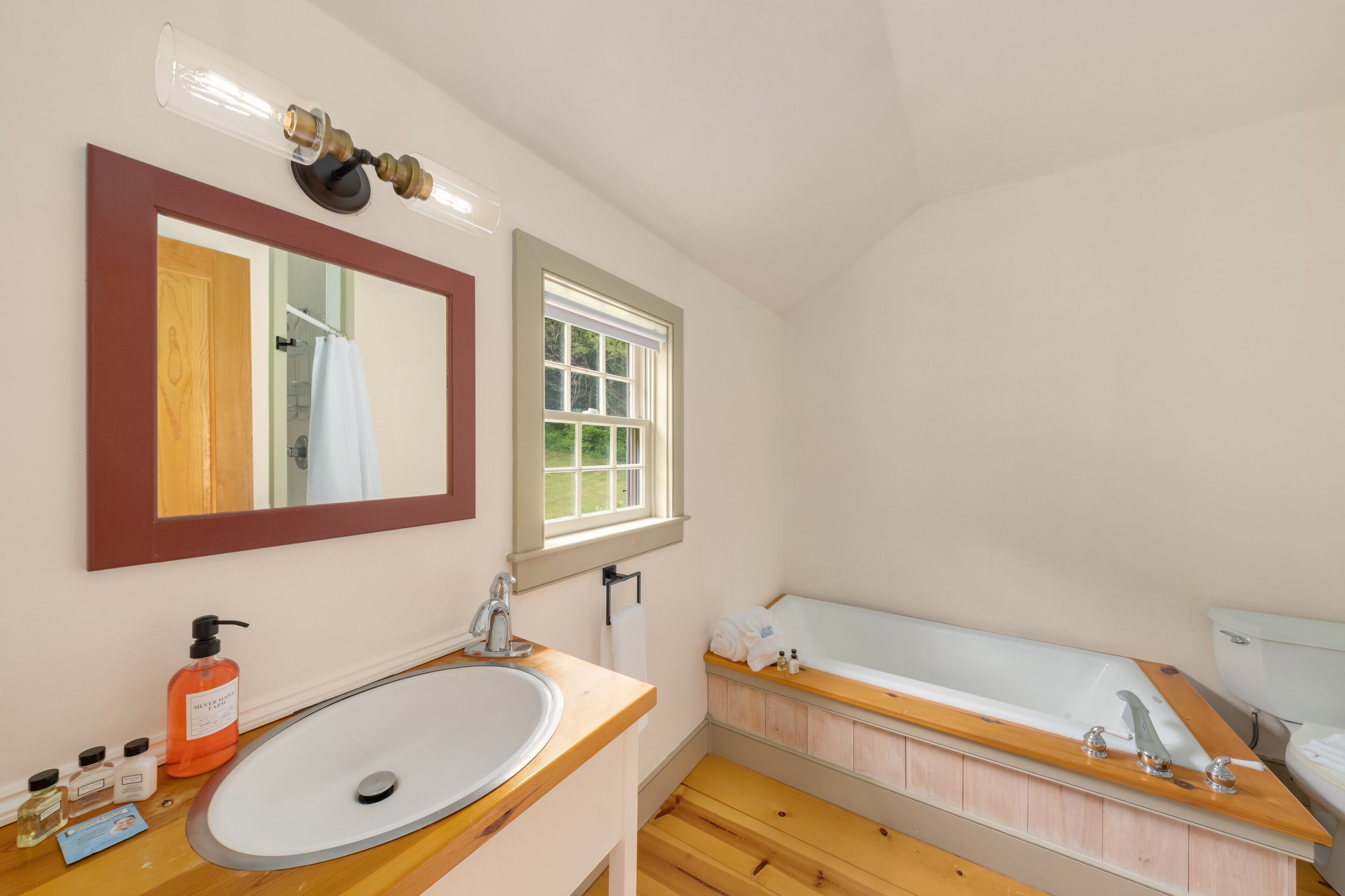A bathroom with a wooden vanity, a large sink, a bathtub, a mirror, and a window.