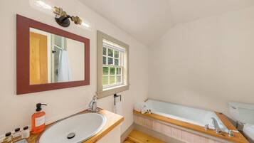 A bathroom with a wooden vanity, a large sink, a bathtub, a mirror, and a window.