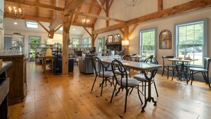 Une cuisine spacieuse avec des poutres en bois, un coin repas doté d’une grande table et de chaises, et une vue sur l’extérieur grâce à de grandes fenêtres.