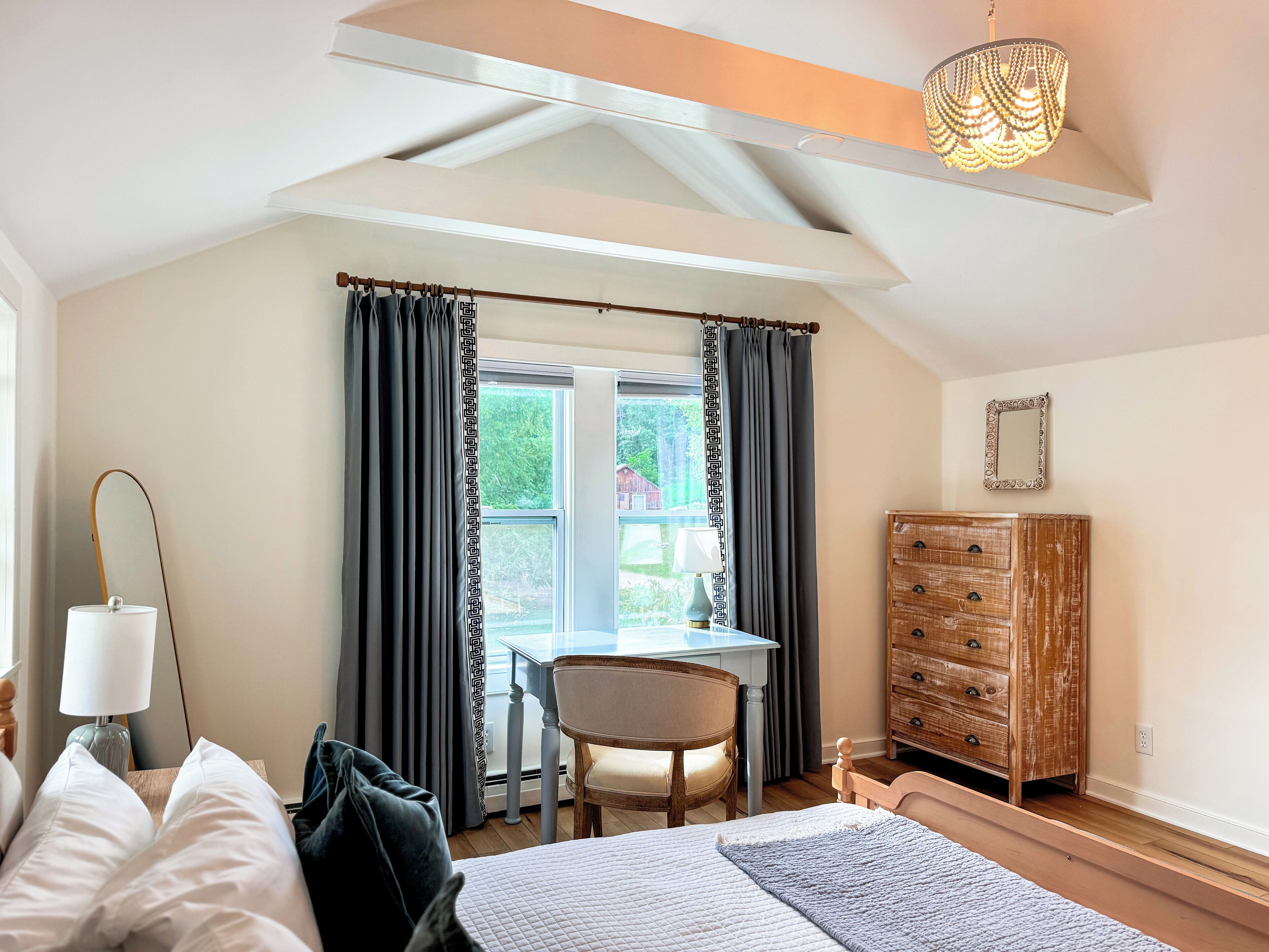 A bedroom with a bed, a desk, a chair, a dresser, and a window with curtains.