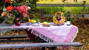 A picnic setup with a table, a basket, a bottle, and a vase with flowers.