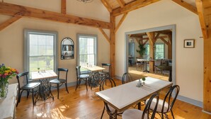 A spacious dining area with wooden beams, large windows, and a view into another room.
