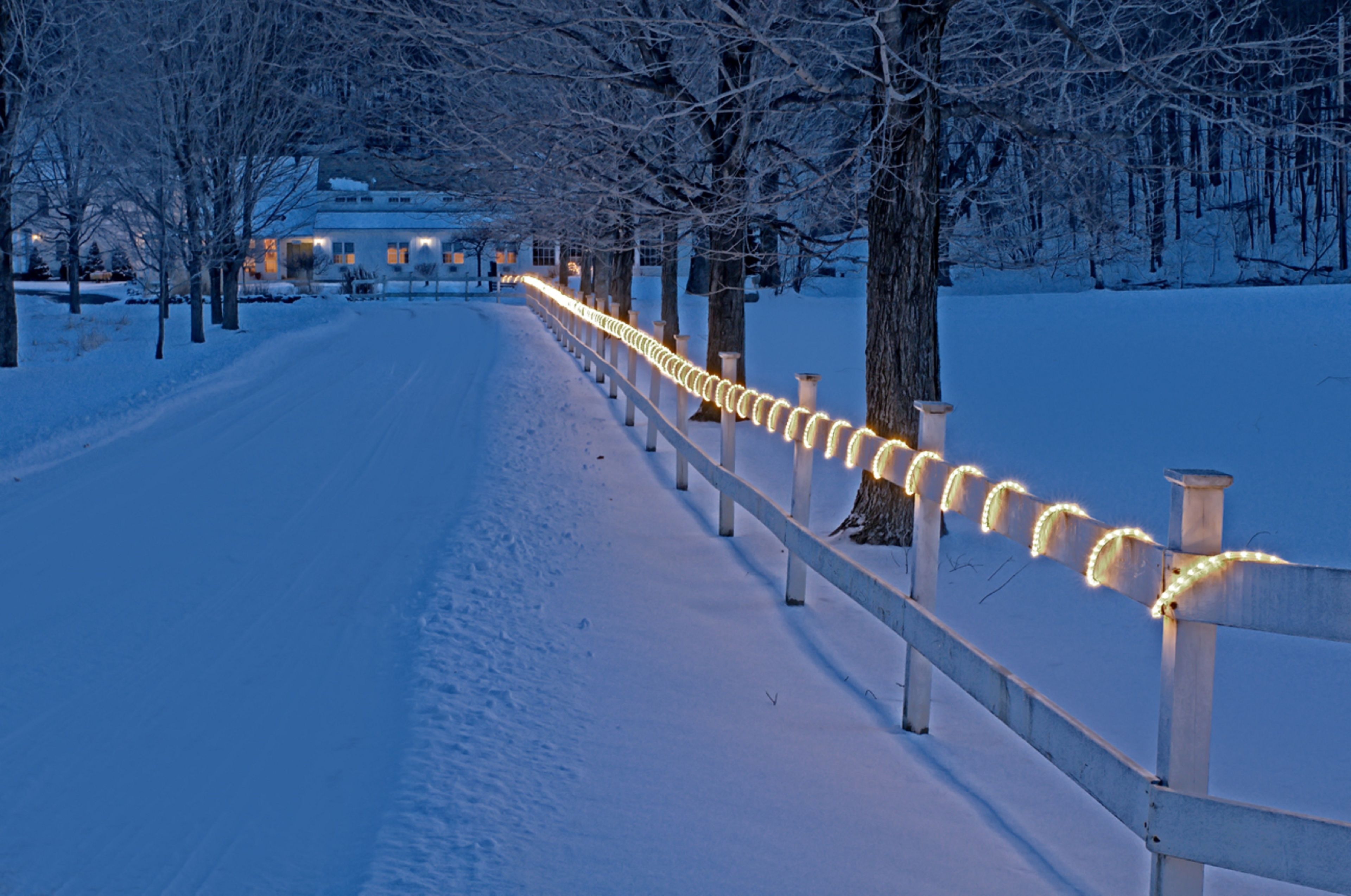 Uma trilha coberta de neve, ladeada por corrimãos iluminados, conduzindo a um edifício.