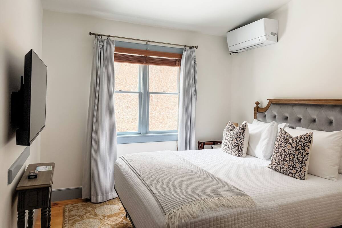 A bedroom with a bed, curtains, a TV, and an air conditioning unit.
