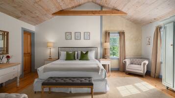 Een slaapkamer met een groot bed, een bankje, een stoel, een nachtkastje en een raam met gordijnen.