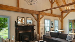 Un salon spacieux avec de hauts plafonds, des poutres apparentes, une cheminée et des sièges confortables.