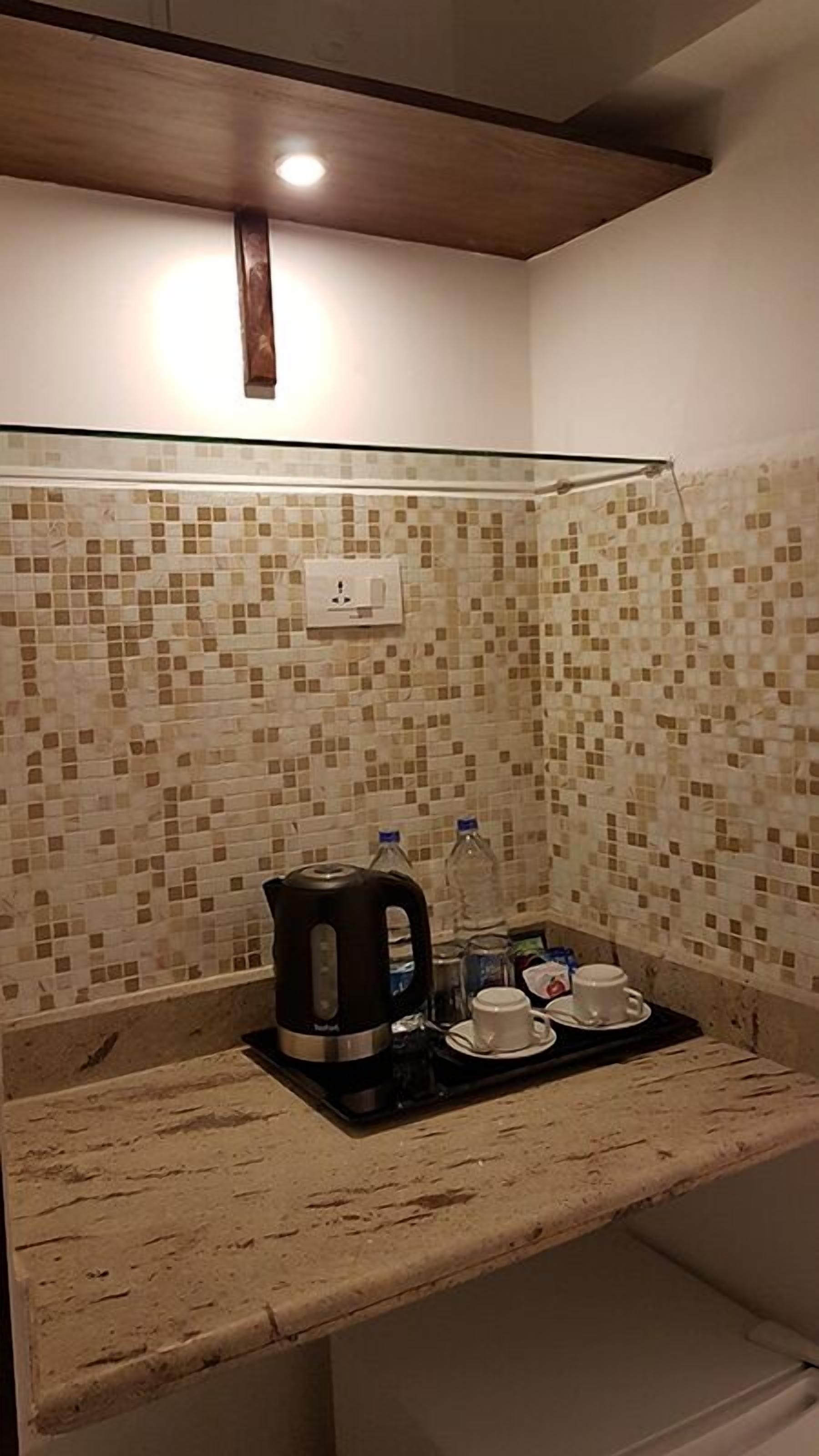 A kitchenette with a tiled backsplash, a coffee maker, cups, and a water bottle.