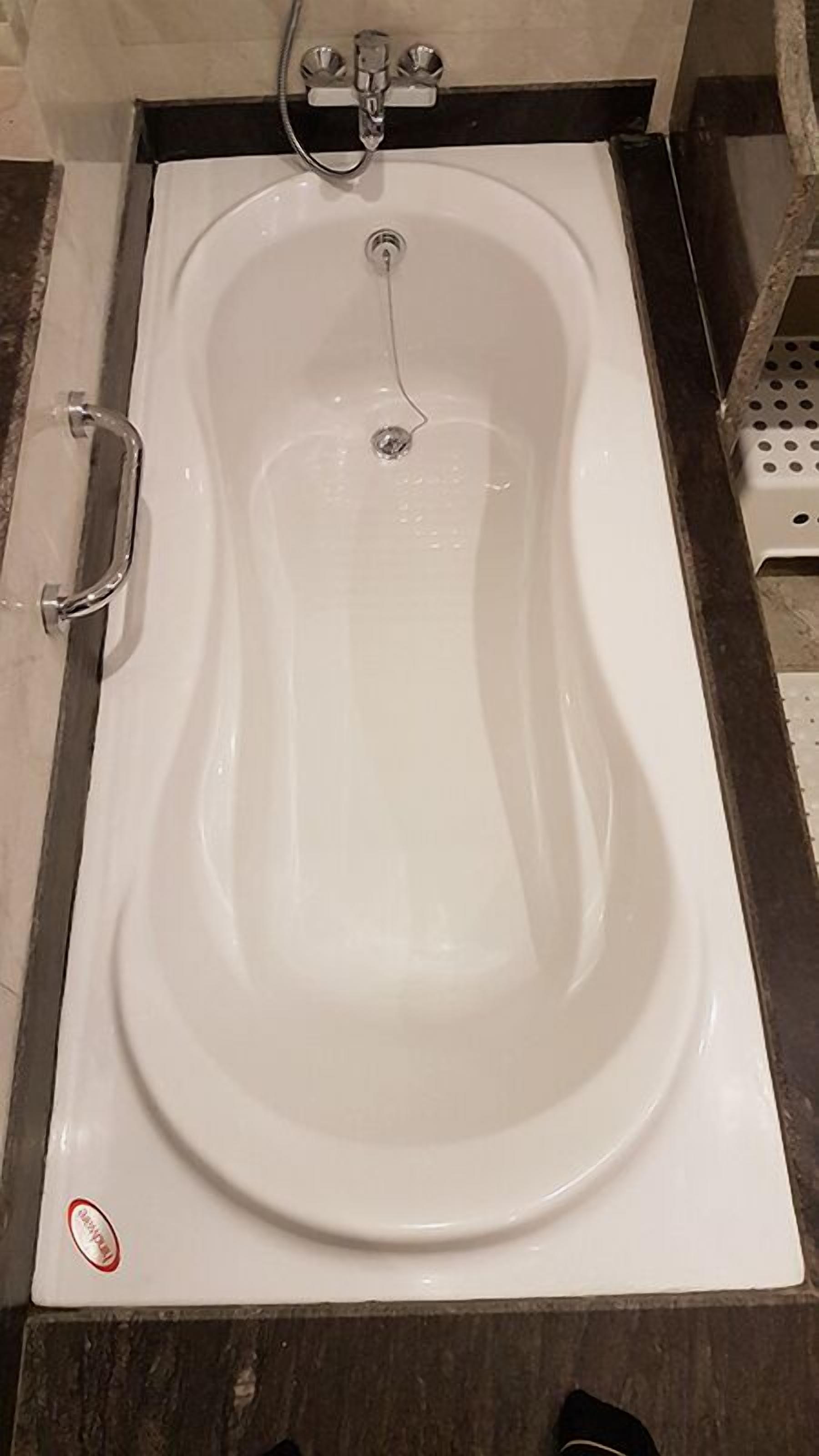 A white bathtub with a faucet and a showerhead, a handrail on the left, and a drain in the center.