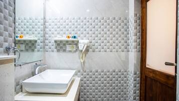 Un baño con un lavamanos blanco, un espejo y un perchero para toallas. Hay una zona de ducha con puerta de cristal y puerta de madera.