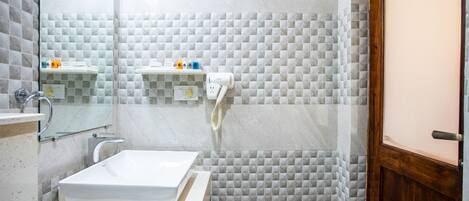 Une salle de bain avec un lavabo blanc, un miroir et un porte-serviettes. Il y a un espace douche avec une porte en verre et une porte en bois.