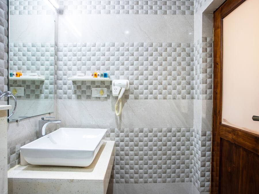 Un baño con un lavamanos blanco, un espejo y un perchero para toallas. Hay una zona de ducha con puerta de cristal y puerta de madera.