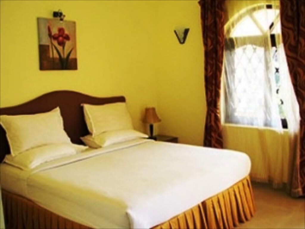 A bed with white linens, a wooden headboard, and a nightstand with a lamp.