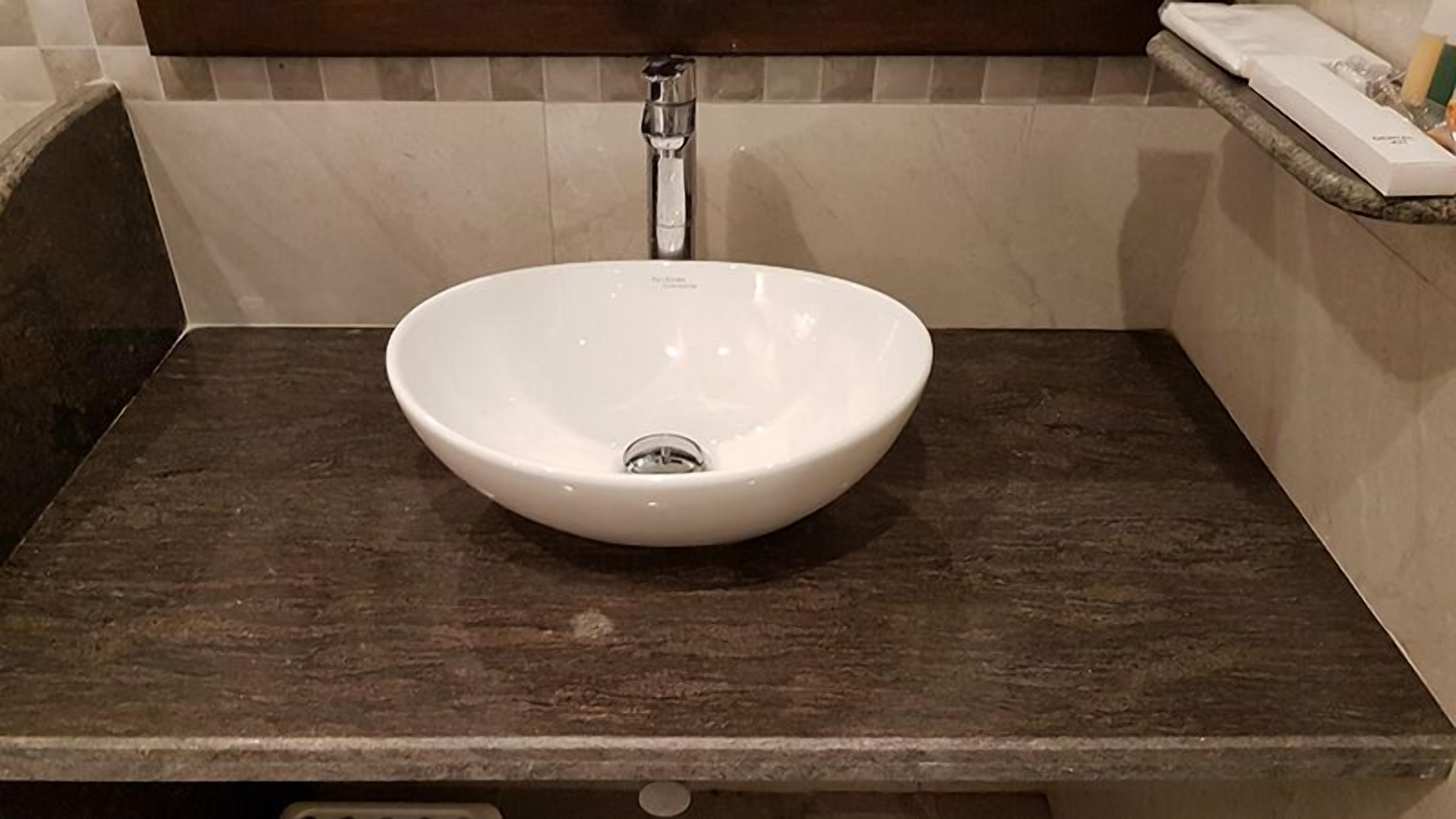 A white vessel sink with a single faucet on a dark countertop in a bathroom.