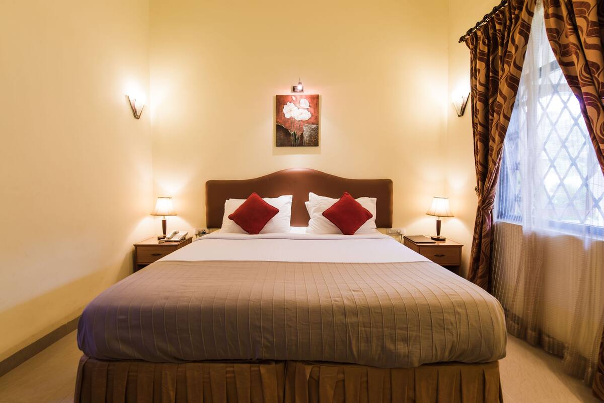 Une chambre d’hôtel avec un grand lit, deux lampes de chevet, une œuvre d’art accrochée au mur et une fenêtre avec des rideaux.
