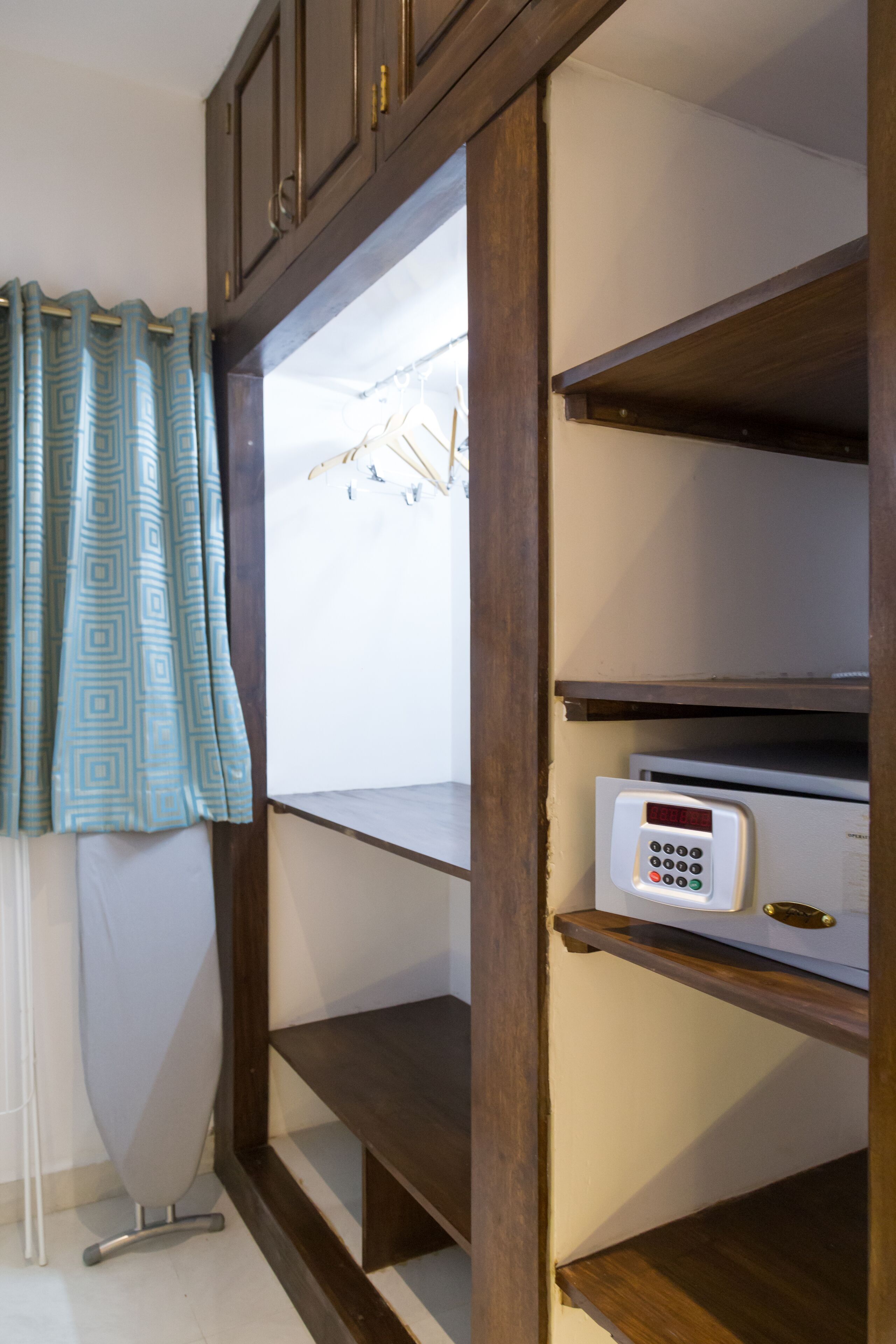 A room with a wooden cabinet, a digital thermostat, and a hanging clothes rack.